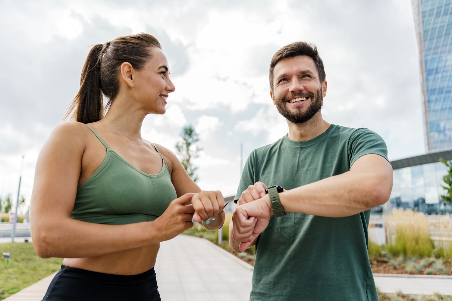 A man and woman in workout attire smile while checking their fitness trackers outdoors - South Bay Endodontics